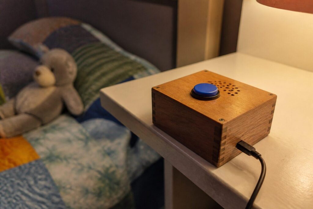 Zelfgebouwd houten kastje met een grote blauwe knop en een luidsprekerrooster op een plank in een kinderkamer